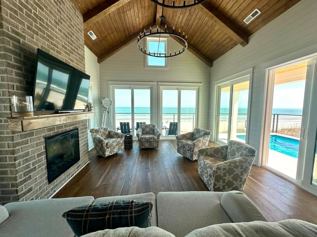 Oceanfront living room with vaulted wood ceiling, fireplace, and beach views, freshly cleaned